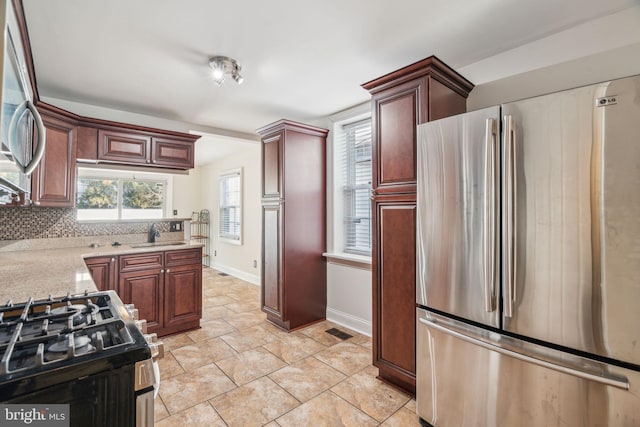 kitchen with light tile patterned flooring, appliances with stainless steel finishes, tasteful backsplash, sink, and light stone countertops