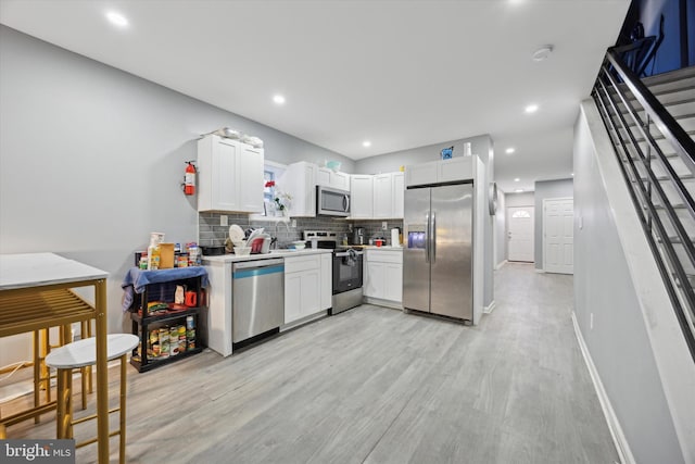 kitchen featuring sink, backsplash, white cabinets, stainless steel appliances, and light wood-type flooring