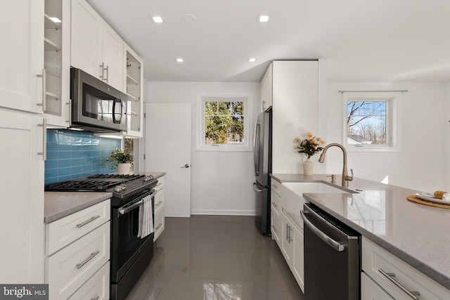 kitchen with sink, appliances with stainless steel finishes, white cabinets, light stone countertops, and backsplash