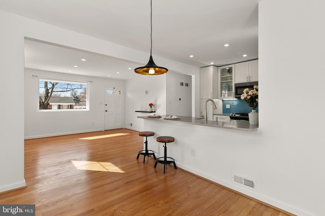 kitchen with sink, white cabinetry, tasteful backsplash, decorative light fixtures, and light wood-type flooring