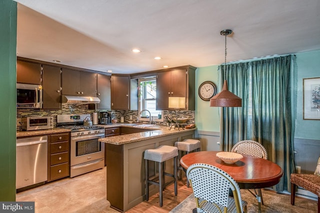 kitchen featuring sink, stone countertops, decorative light fixtures, appliances with stainless steel finishes, and kitchen peninsula