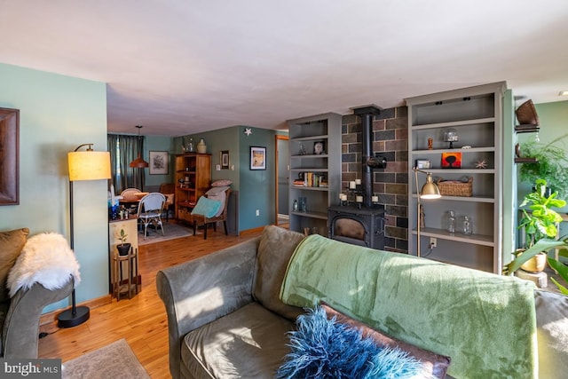 living room with built in shelves, a wood stove, and light hardwood / wood-style flooring