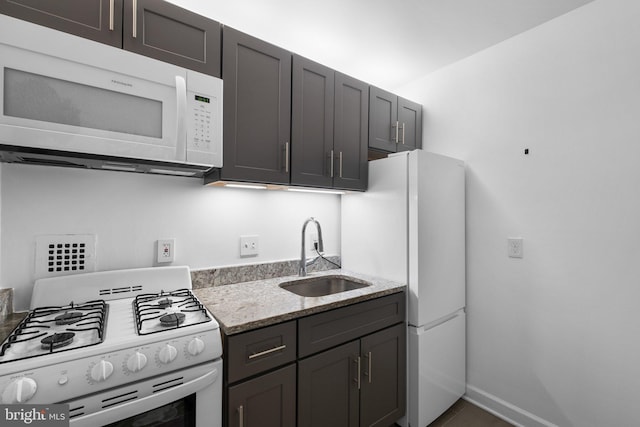 kitchen featuring sink, white appliances, dark brown cabinets, and light stone countertops