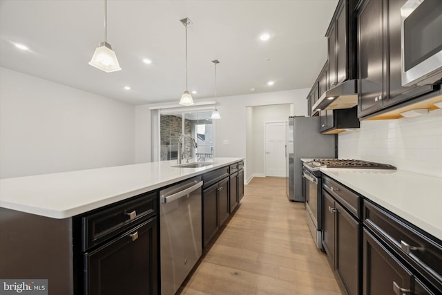 kitchen featuring appliances with stainless steel finishes, pendant lighting, sink, decorative backsplash, and light wood-type flooring