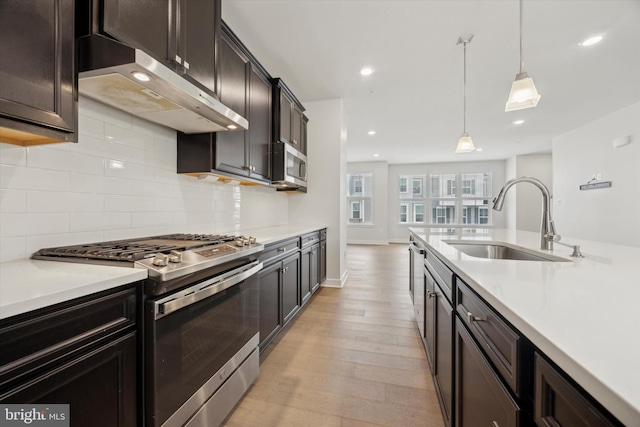 kitchen with appliances with stainless steel finishes, decorative light fixtures, tasteful backsplash, sink, and light wood-type flooring