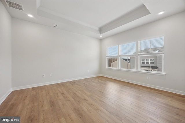 empty room featuring a tray ceiling and light wood-type flooring