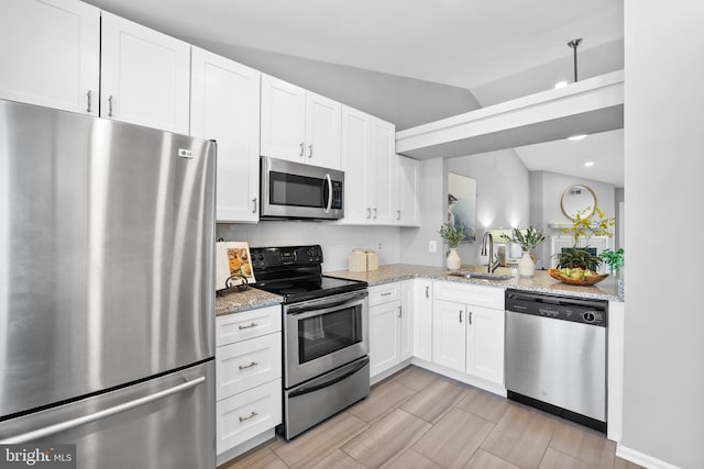 kitchen with lofted ceiling, sink, appliances with stainless steel finishes, light stone countertops, and white cabinets