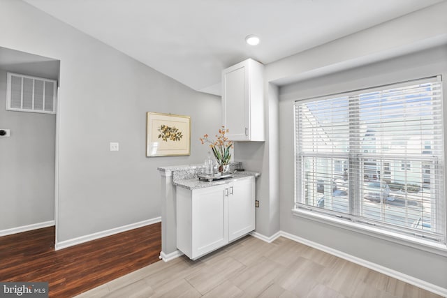 kitchen featuring vaulted ceiling, white cabinetry, and light stone countertops