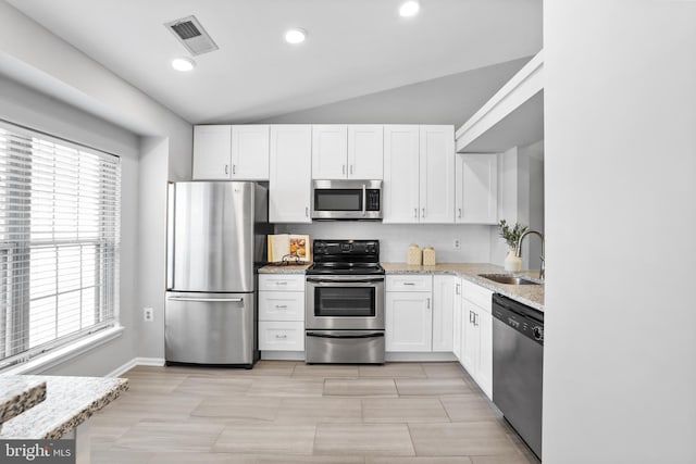 kitchen featuring lofted ceiling, sink, stainless steel appliances, light stone countertops, and white cabinets