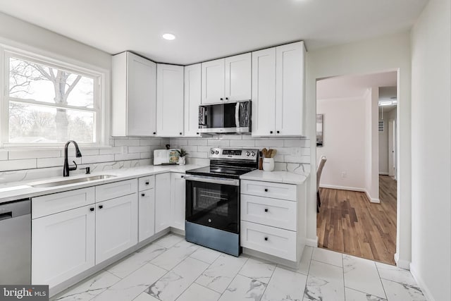 kitchen with marble finish floor, appliances with stainless steel finishes, white cabinetry, and a sink