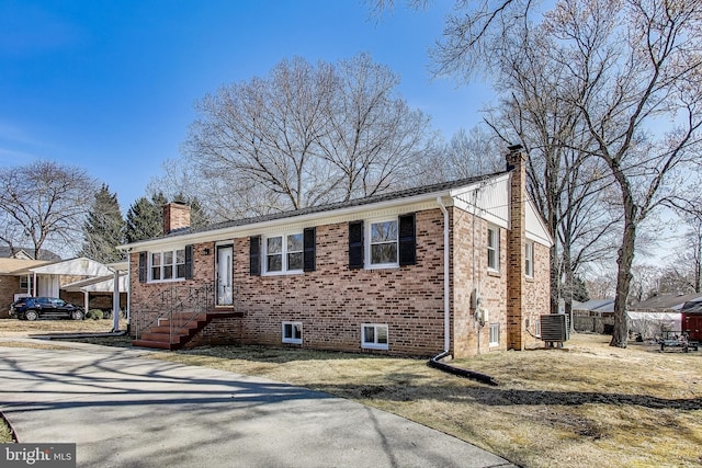 view of front of home with cooling unit, a front lawn, brick siding, and a chimney