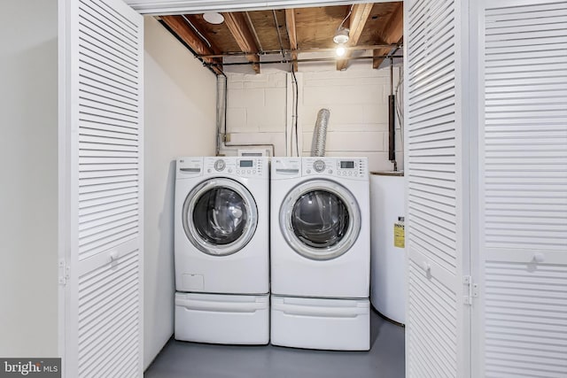 clothes washing area with electric water heater, washing machine and dryer, concrete block wall, and laundry area