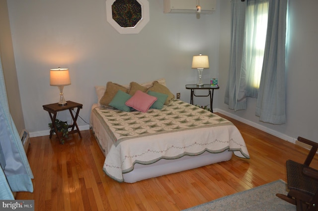 bedroom featuring wood-type flooring and an AC wall unit