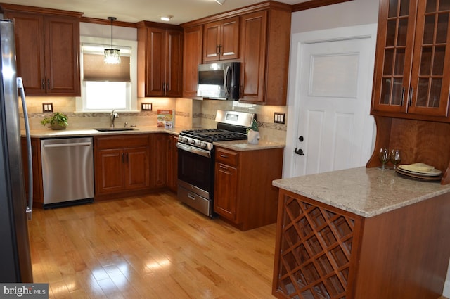 kitchen featuring pendant lighting, sink, appliances with stainless steel finishes, backsplash, and light hardwood / wood-style floors