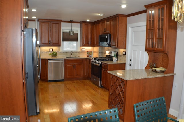 kitchen with decorative light fixtures, backsplash, stainless steel appliances, light stone countertops, and light wood-type flooring