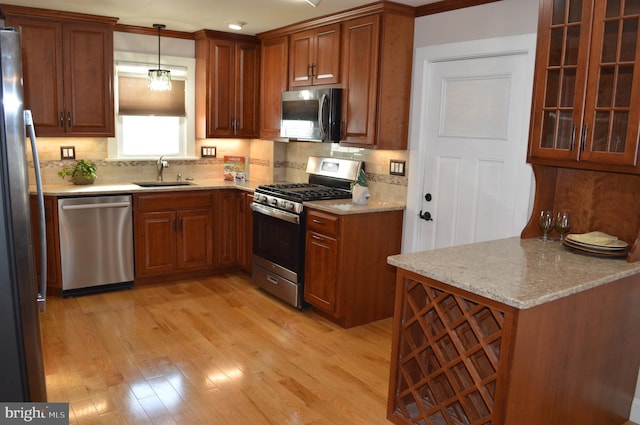 kitchen with stainless steel appliances, sink, light hardwood / wood-style flooring, and decorative light fixtures