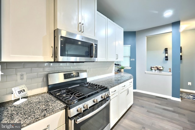 kitchen featuring stainless steel appliances, wood-type flooring, white cabinets, and dark stone counters