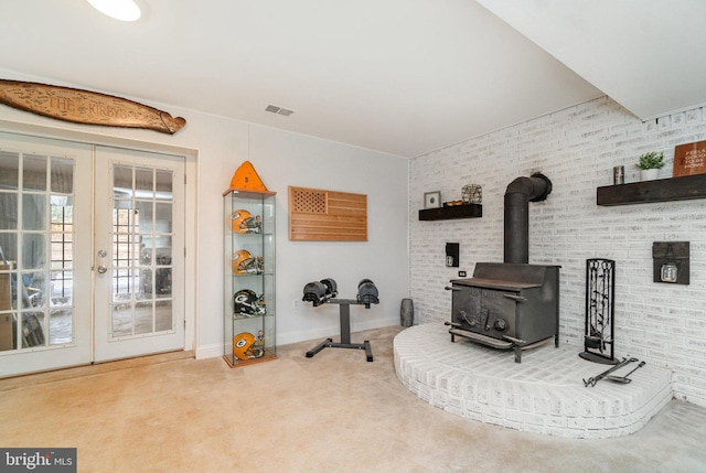 exercise room with a wood stove, french doors, brick wall, and carpet flooring