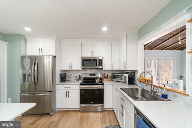 kitchen featuring sink, white cabinetry, stainless steel appliances, light hardwood / wood-style floors, and decorative backsplash