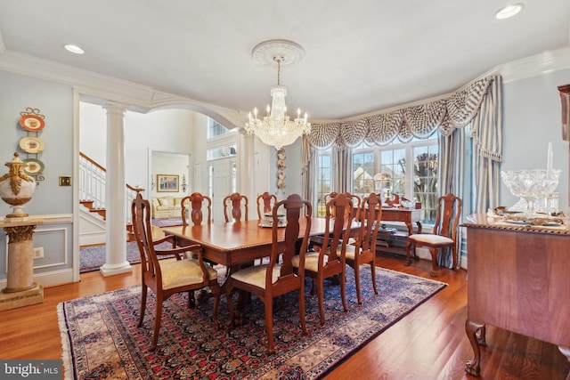 dining space featuring wood-type flooring, ornamental molding, a chandelier, and ornate columns