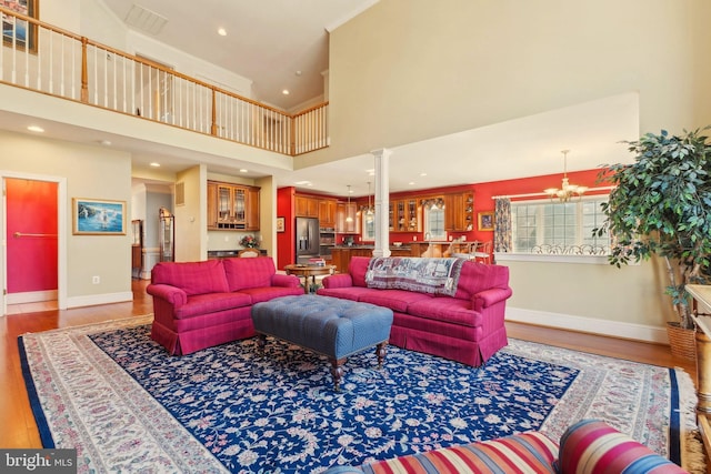 living room featuring an inviting chandelier, hardwood / wood-style flooring, decorative columns, and a towering ceiling