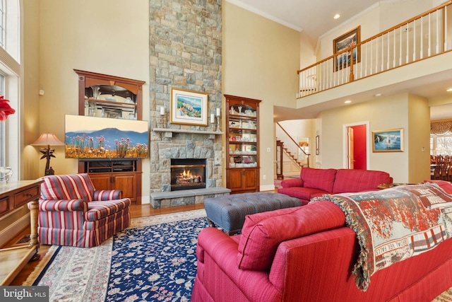 living room with wood-type flooring, crown molding, a fireplace, and a towering ceiling