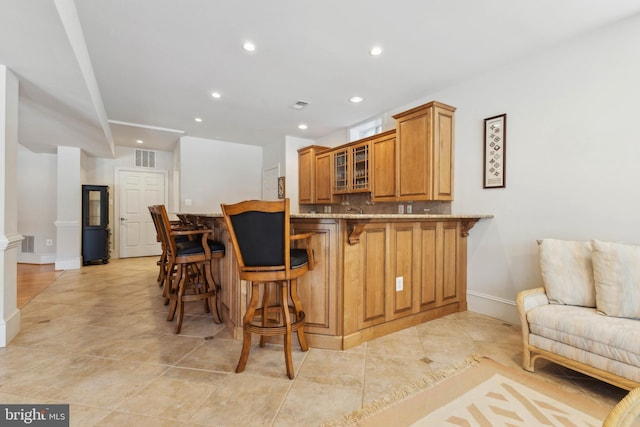 kitchen featuring a breakfast bar, backsplash, light tile patterned floors, kitchen peninsula, and light stone countertops