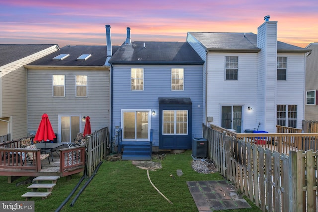 back house at dusk with a yard, central AC unit, and a deck