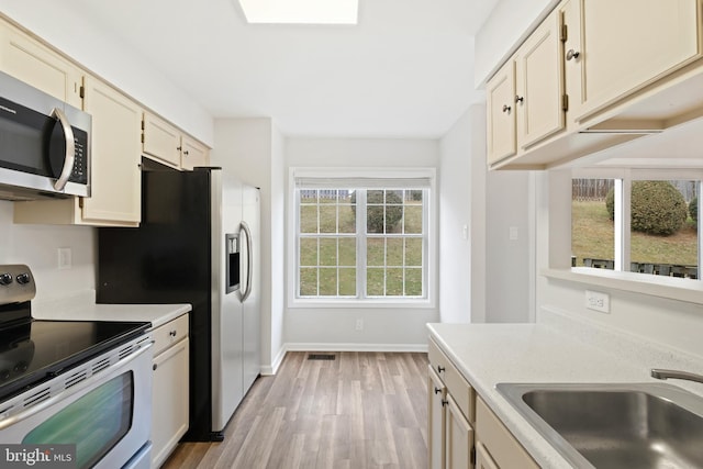 kitchen featuring sink, cream cabinets, light hardwood / wood-style floors, and appliances with stainless steel finishes