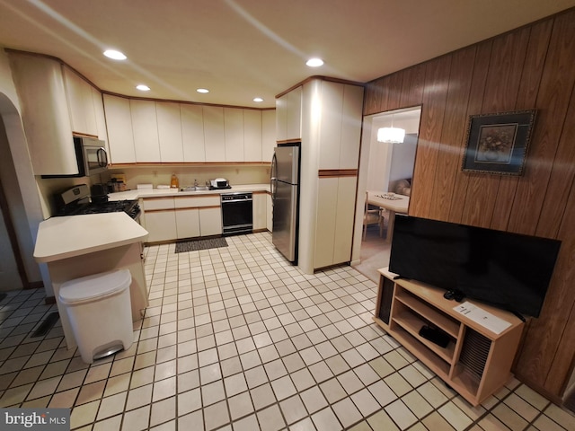 kitchen featuring appliances with stainless steel finishes, wooden walls, sink, white cabinets, and light tile patterned floors