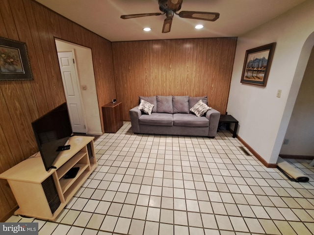 tiled living room featuring ceiling fan and wood walls