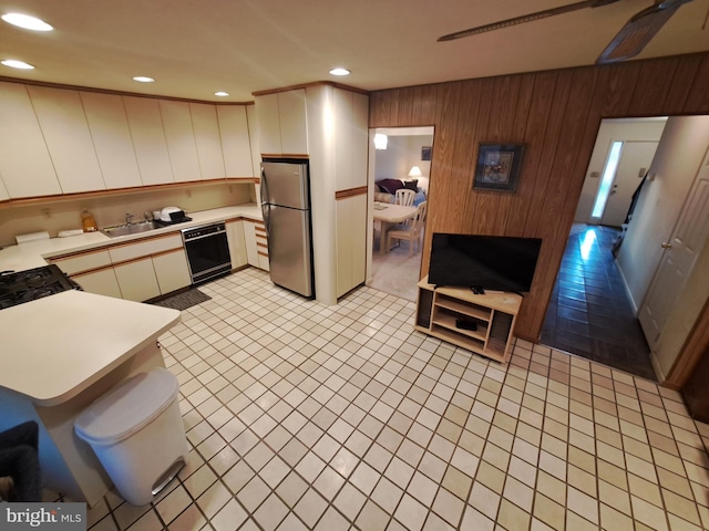 kitchen with sink, kitchen peninsula, wood walls, and black appliances