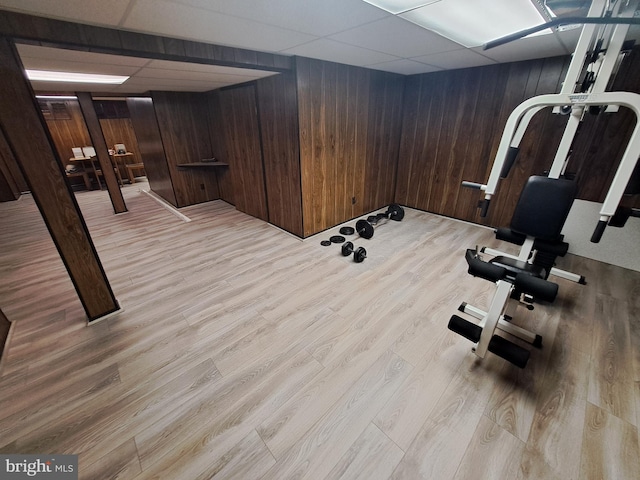 workout room featuring a paneled ceiling, light wood-type flooring, and wood walls