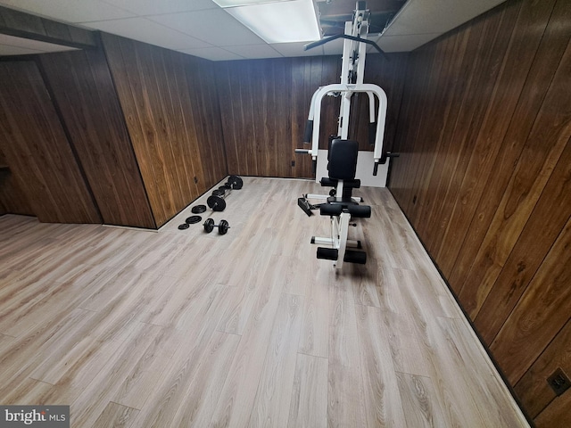 exercise room with a drop ceiling, light hardwood / wood-style floors, and wood walls