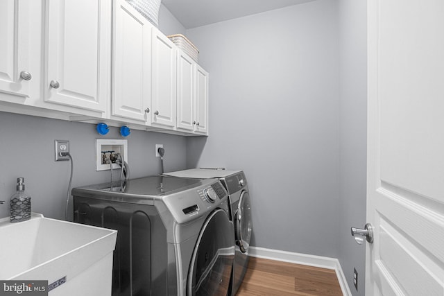 clothes washing area with sink, hardwood / wood-style flooring, cabinets, and washing machine and clothes dryer