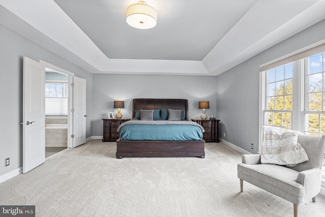 bedroom with ensuite bath, a tray ceiling, and light carpet