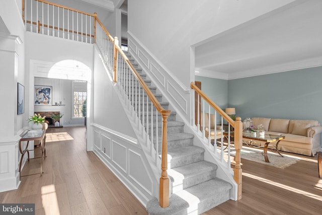 staircase with wood-type flooring, crown molding, and a fireplace