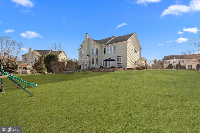 back of property with a gazebo, a lawn, and a playground