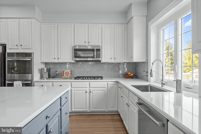 kitchen with sink, white cabinetry, backsplash, stainless steel appliances, and light hardwood / wood-style floors