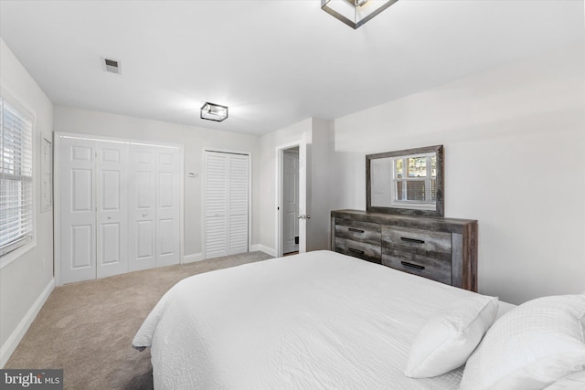 bedroom with multiple closets, light colored carpet, and multiple windows