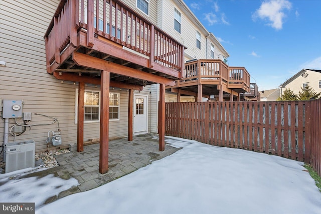 snow covered house with central AC, a wooden deck, and a patio area