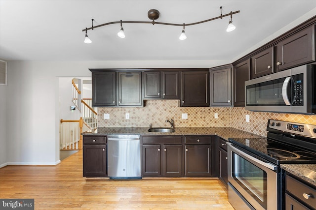 kitchen featuring sink, light hardwood / wood-style flooring, appliances with stainless steel finishes, dark stone countertops, and dark brown cabinetry