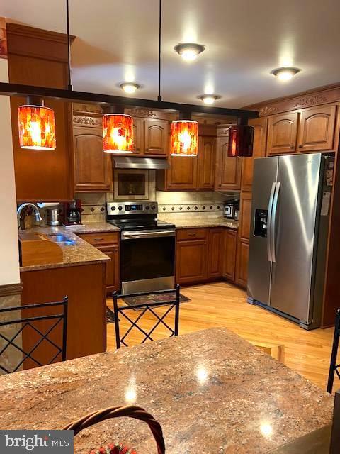 kitchen featuring sink, appliances with stainless steel finishes, light stone countertops, light hardwood / wood-style floors, and decorative light fixtures