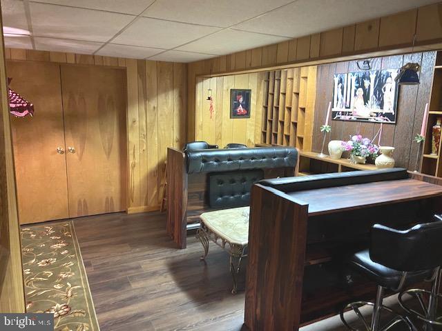 recreation room with dark wood-type flooring, a paneled ceiling, and wooden walls