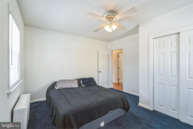 bedroom with ceiling fan, radiator, dark carpet, and a closet