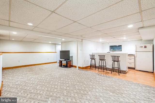 basement with indoor bar, a paneled ceiling, and white refrigerator