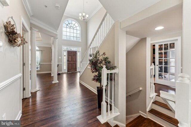 foyer entrance featuring decorative columns, crown molding, dark wood-type flooring, and a chandelier