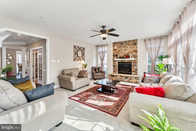 living room featuring a stone fireplace, ornamental molding, carpet floors, ceiling fan, and decorative columns