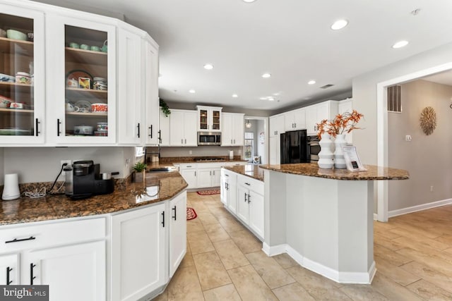 kitchen featuring sink, appliances with stainless steel finishes, dark stone countertops, white cabinetry, and a center island