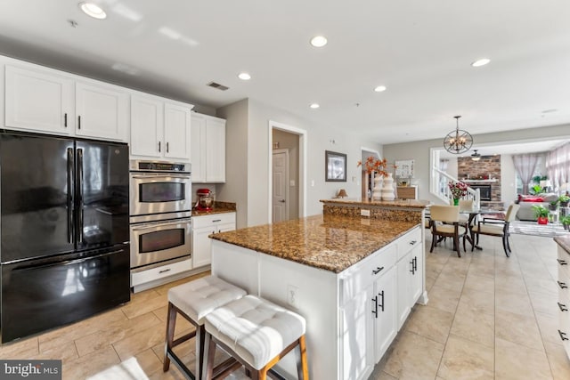 kitchen with white cabinetry, a center island, stainless steel double oven, and black fridge